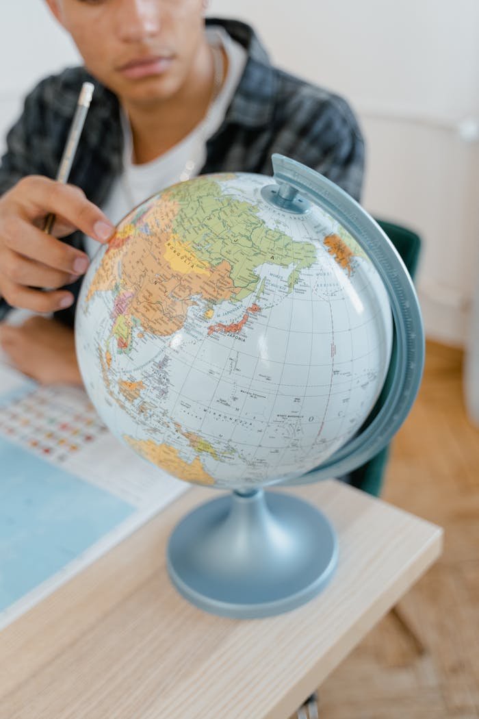 A student pointing at a globe in a classroom setting, emphasizing geography and learning.